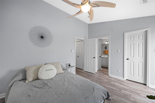 bedroom featuring visible vents, ensuite bathroom, wood finished floors, baseboards, and lofted ceiling