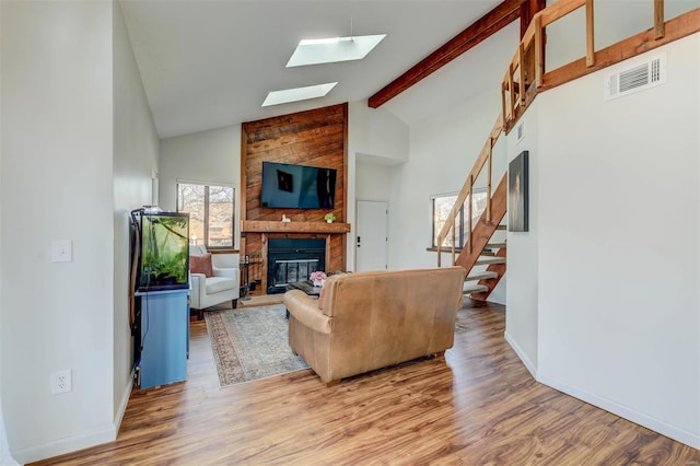 living room with visible vents, beam ceiling, wood finished floors, a large fireplace, and a skylight