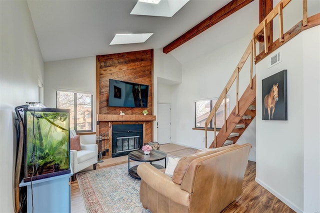 living room with visible vents, beam ceiling, a fireplace, a skylight, and wood finished floors