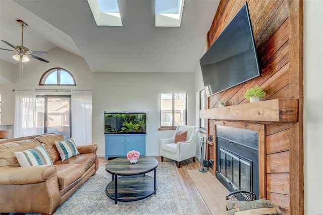 living room featuring a glass covered fireplace, lofted ceiling with skylight, light wood finished floors, and a wealth of natural light