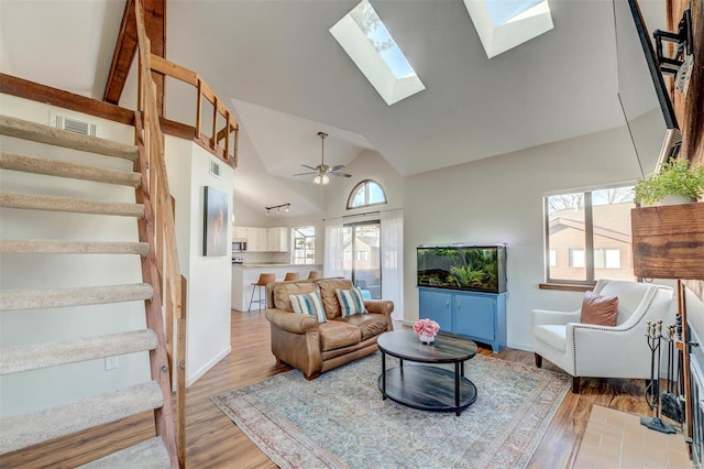 living area with a skylight, visible vents, light wood-type flooring, and high vaulted ceiling