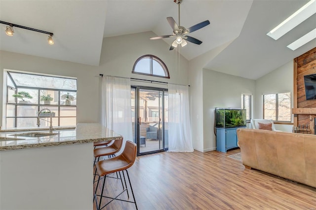 kitchen featuring light stone countertops, light wood-type flooring, a kitchen breakfast bar, a skylight, and a sink