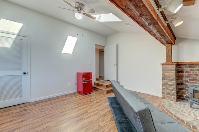 interior space with vaulted ceiling, a wood stove, a ceiling fan, and light wood finished floors