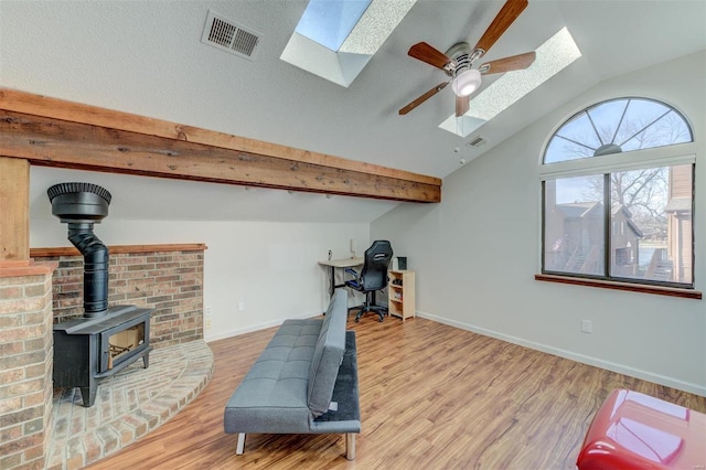 workout room featuring visible vents, baseboards, vaulted ceiling with skylight, a wood stove, and wood finished floors