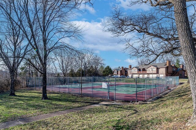 view of tennis court with a yard and fence