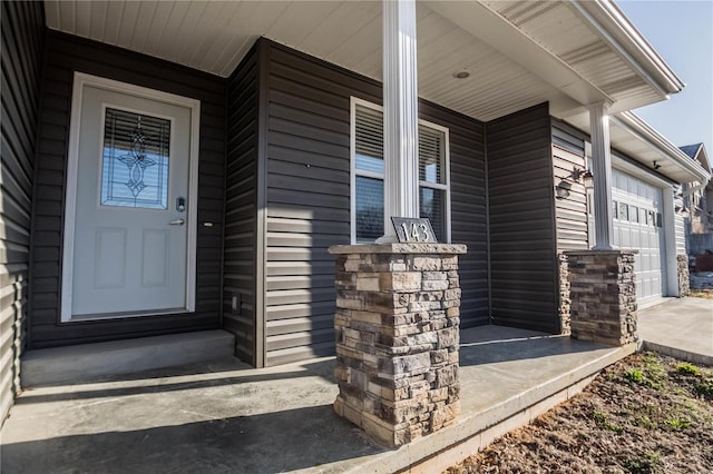 entrance to property with a garage, stone siding, and covered porch