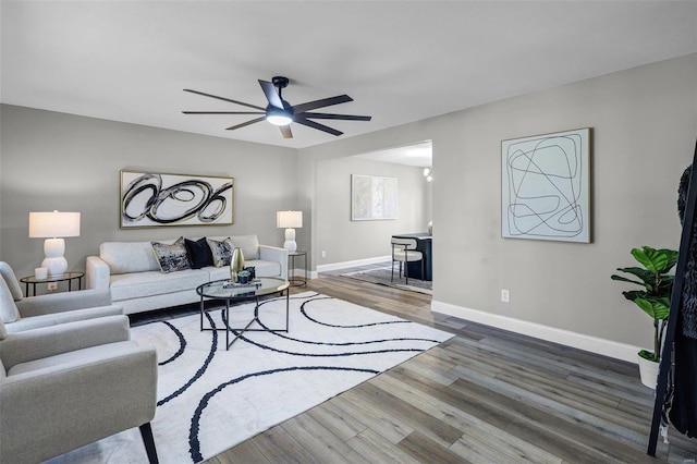 living room with a ceiling fan, baseboards, and wood finished floors