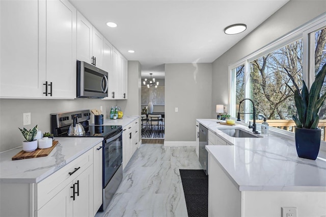 kitchen featuring light stone counters, an inviting chandelier, a sink, appliances with stainless steel finishes, and white cabinetry