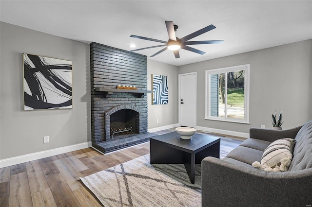 living area featuring ceiling fan, a brick fireplace, baseboards, and wood finished floors