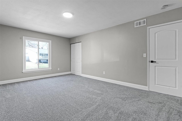 spare room with carpet flooring, baseboards, visible vents, and a textured ceiling