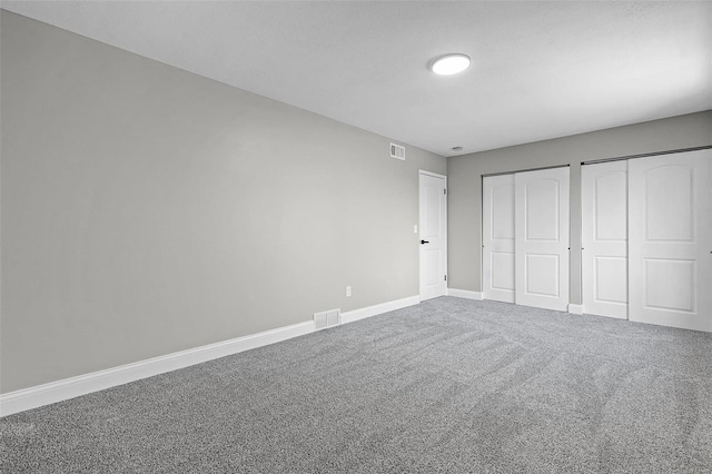 unfurnished bedroom featuring carpet flooring, baseboards, visible vents, and two closets