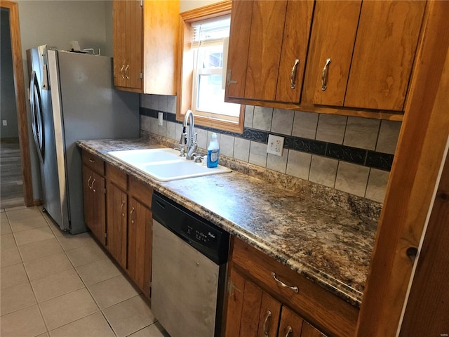 kitchen with light tile patterned floors, a sink, stainless steel appliances, tasteful backsplash, and brown cabinets