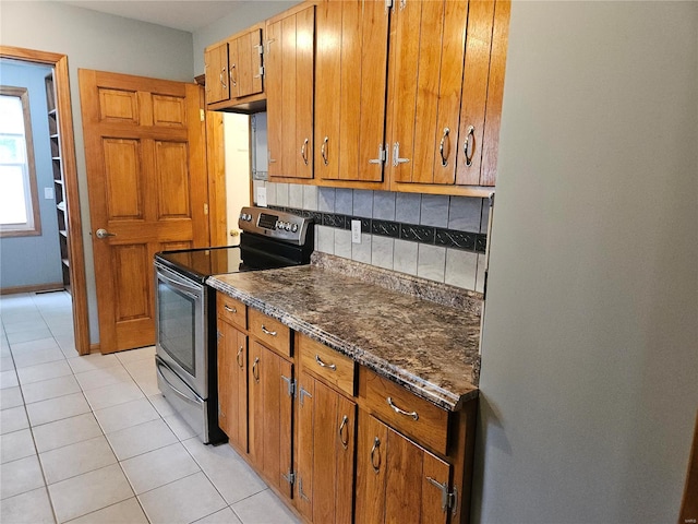 kitchen with brown cabinetry, light tile patterned flooring, freestanding refrigerator, stainless steel range with electric cooktop, and decorative backsplash