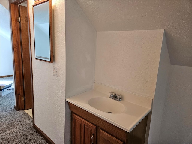 bathroom featuring a textured ceiling, vanity, lofted ceiling, and a textured wall