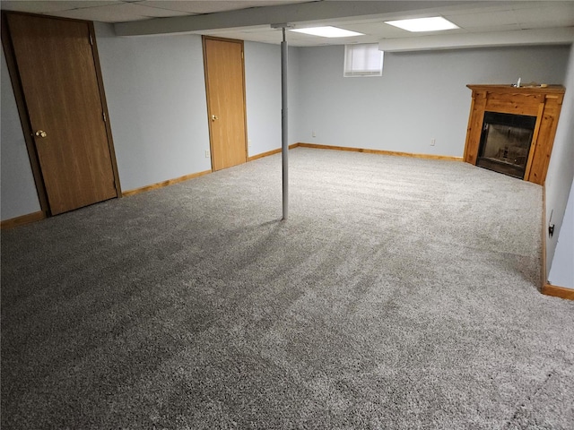 below grade area with carpet flooring, a fireplace, baseboards, and a paneled ceiling