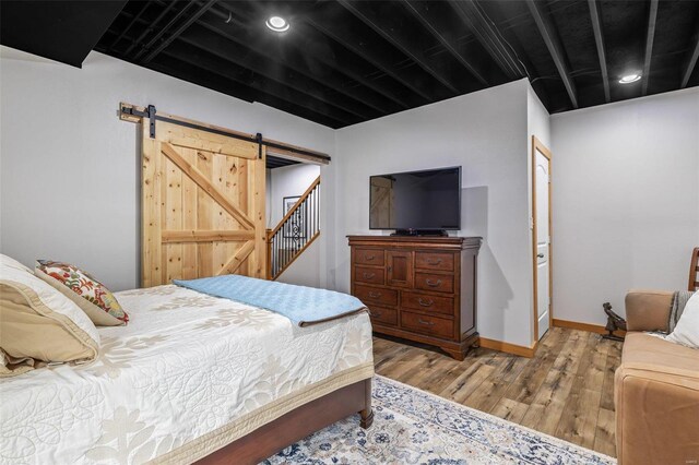 bedroom featuring recessed lighting, a barn door, baseboards, and wood finished floors