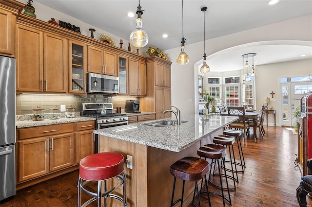 kitchen with tasteful backsplash, brown cabinets, appliances with stainless steel finishes, arched walkways, and a sink