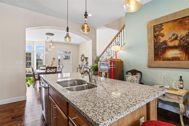 kitchen with a sink, decorative light fixtures, arched walkways, and dark wood finished floors