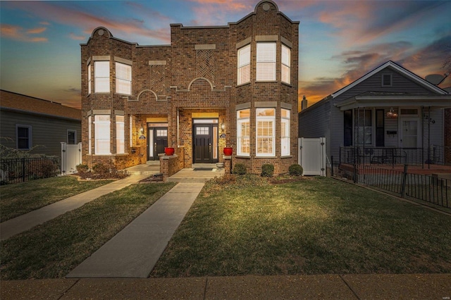 view of front of house with a gate, fence, brick siding, and a lawn