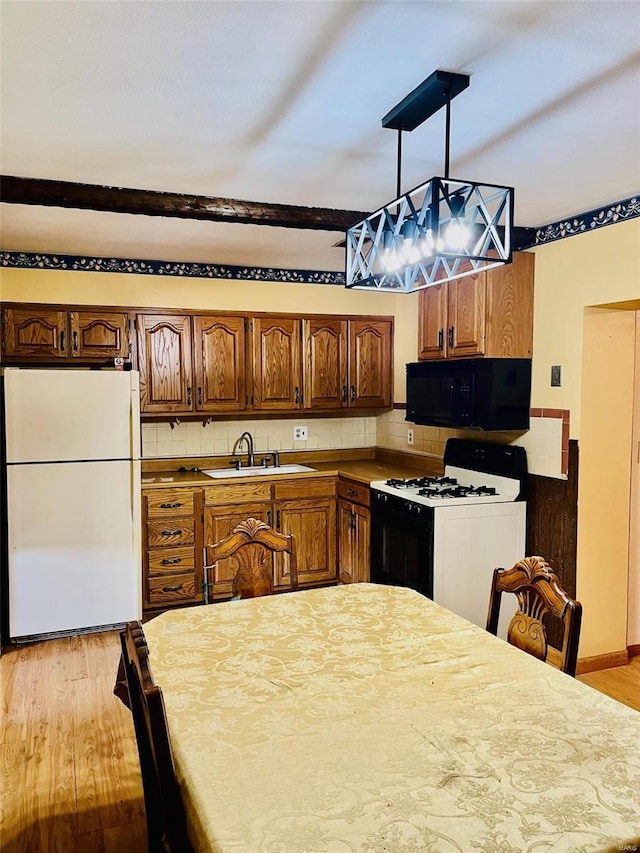 kitchen featuring black microwave, gas range, light wood-style flooring, freestanding refrigerator, and a sink