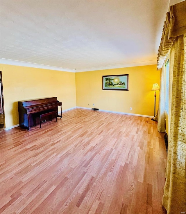 unfurnished room with crown molding, light wood-style flooring, visible vents, and baseboards