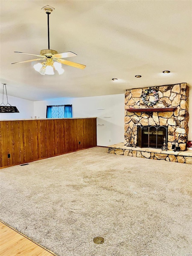 carpeted living area with a wainscoted wall, a textured ceiling, wood walls, a fireplace, and ceiling fan