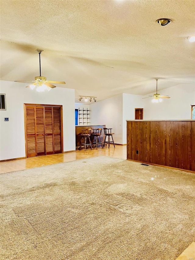 living area featuring visible vents, vaulted ceiling, rail lighting, a textured ceiling, and a ceiling fan