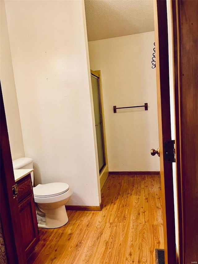 bathroom with visible vents, toilet, wood finished floors, a shower stall, and baseboards