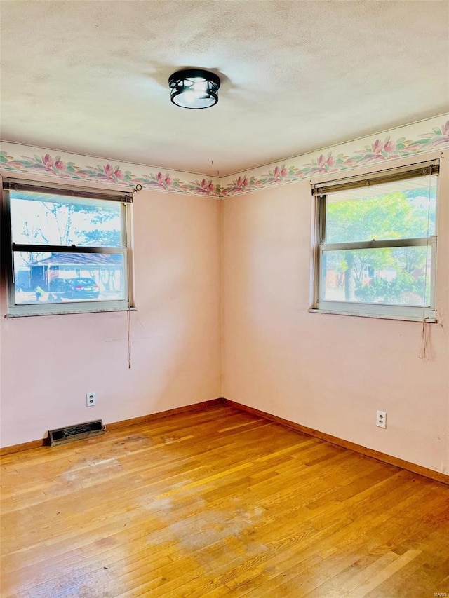 unfurnished room with baseboards, visible vents, light wood finished floors, and a textured ceiling