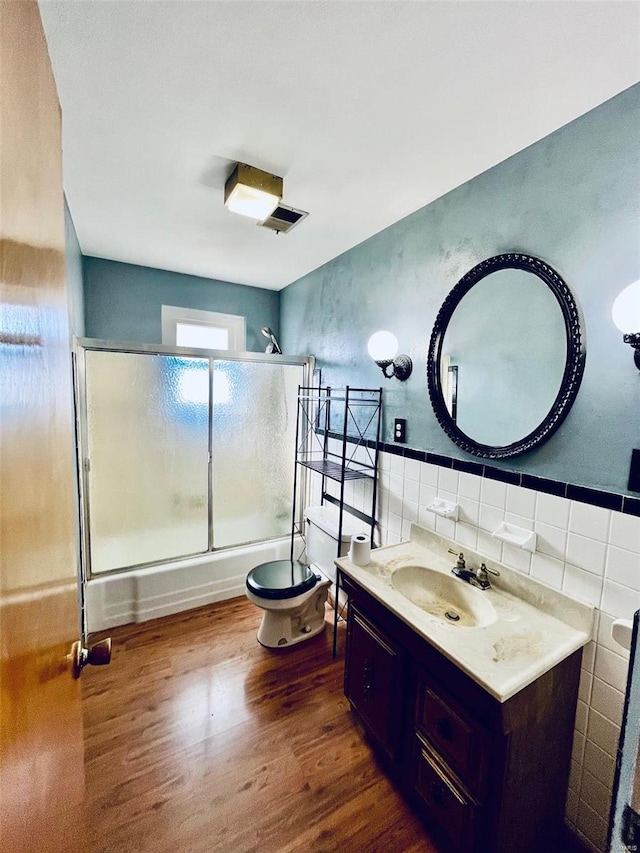 bathroom with toilet, vanity, wood finished floors, enclosed tub / shower combo, and tile walls