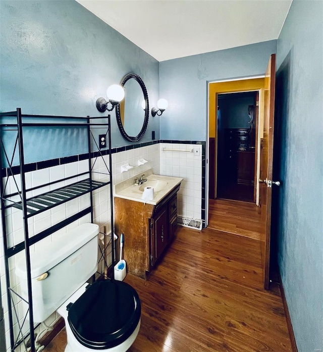 bathroom featuring toilet, wood finished floors, tile walls, wainscoting, and vanity