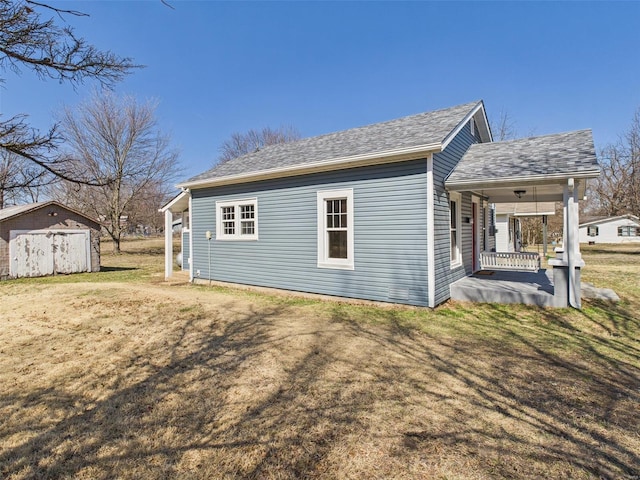 view of side of home with a yard, an outbuilding, covered porch, and a shingled roof