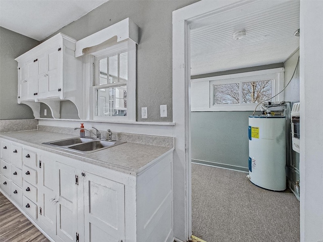 kitchen with a sink, white cabinetry, a wealth of natural light, and electric water heater