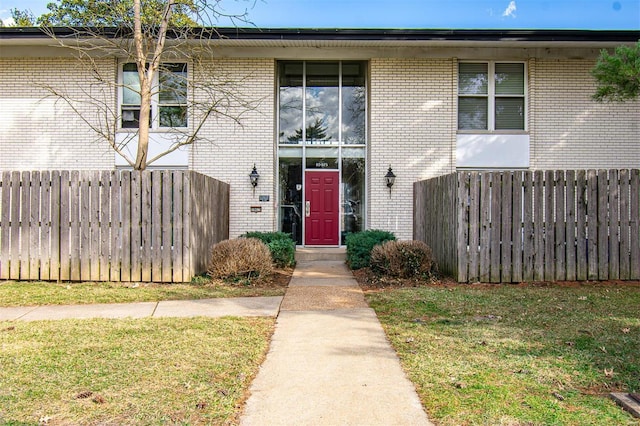 view of exterior entry featuring brick siding and fence