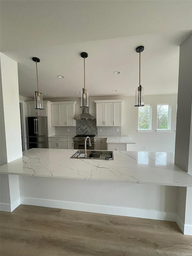 kitchen with light stone counters, wood finished floors, a sink, high end appliances, and wall chimney exhaust hood