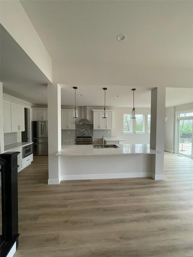 kitchen featuring light wood-type flooring, stainless steel appliances, recessed lighting, and wall chimney range hood