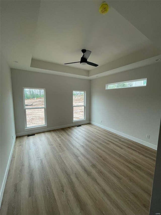 spare room with a ceiling fan, wood finished floors, a raised ceiling, baseboards, and visible vents