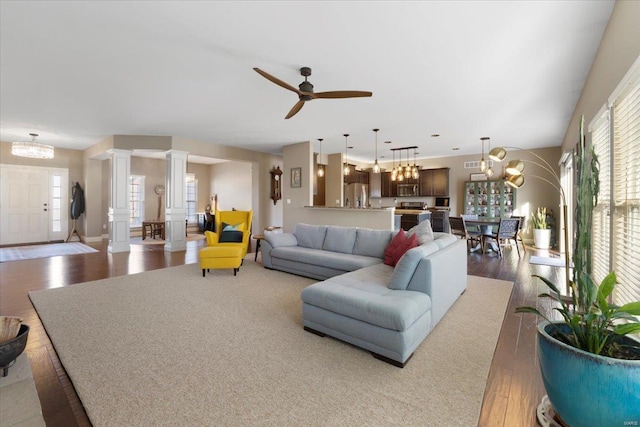 living room featuring decorative columns, wood finished floors, and ceiling fan with notable chandelier