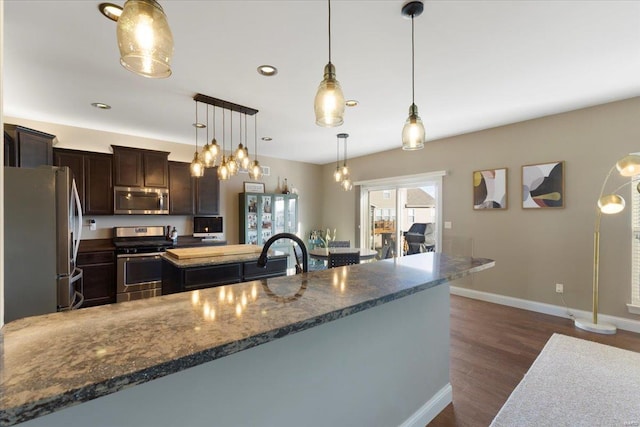 kitchen with baseboards, dark wood finished floors, stainless steel appliances, hanging light fixtures, and dark brown cabinets