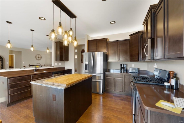 kitchen featuring a sink, dark wood-style floors, stainless steel appliances, dark brown cabinetry, and a peninsula