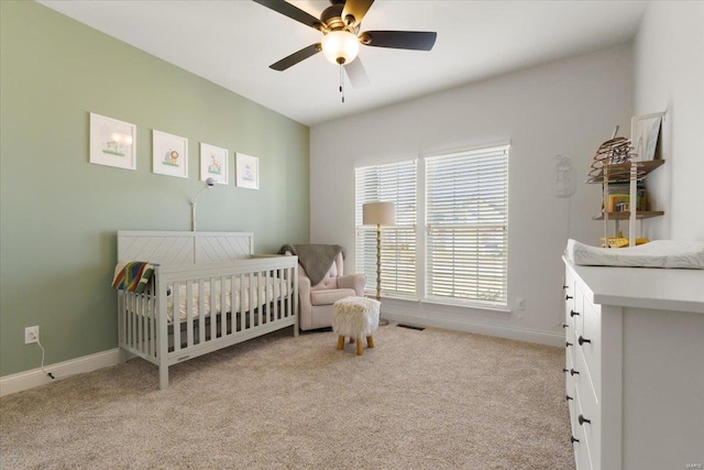 bedroom with visible vents, a crib, baseboards, light carpet, and a ceiling fan