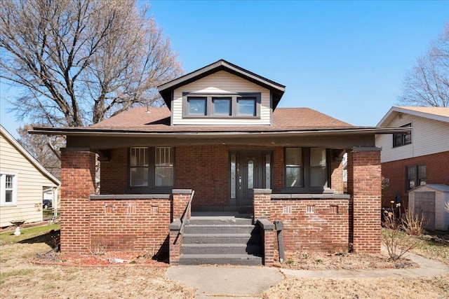 bungalow-style home with brick siding, a porch, a storage unit, and an outbuilding