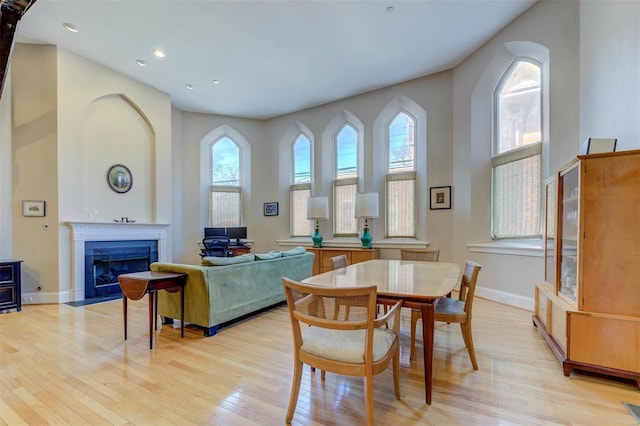 dining room featuring light wood finished floors, a fireplace with flush hearth, recessed lighting, and baseboards