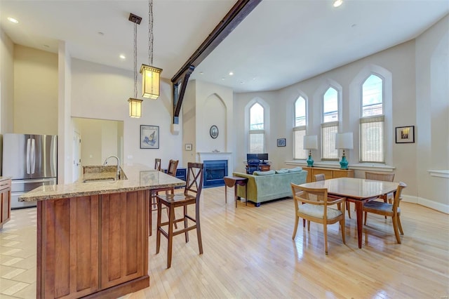 kitchen featuring light wood-style flooring, a sink, light stone counters, freestanding refrigerator, and a fireplace