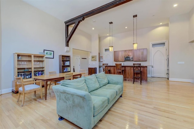 living room featuring baseboards, light wood-style floors, and a towering ceiling