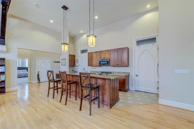 kitchen featuring stainless steel microwave, a breakfast bar, a high ceiling, light wood-style floors, and hanging light fixtures