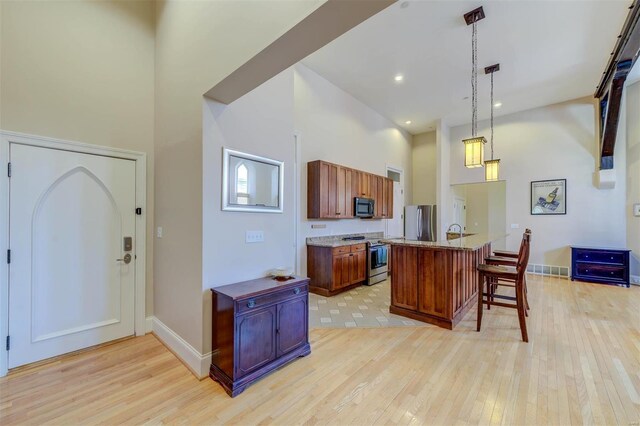 kitchen featuring light wood-type flooring, a breakfast bar, stainless steel appliances, a high ceiling, and hanging light fixtures