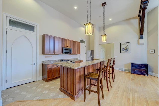 kitchen featuring light wood-type flooring, a breakfast bar area, stainless steel appliances, and a high ceiling