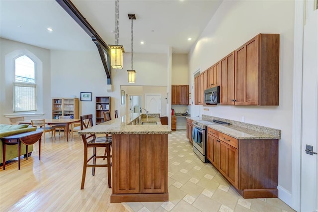 kitchen featuring a high ceiling, a sink, hanging light fixtures, appliances with stainless steel finishes, and a kitchen bar