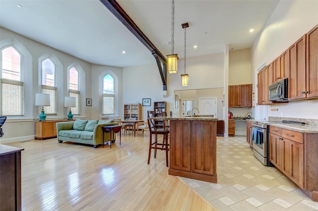 kitchen with decorative light fixtures, a breakfast bar area, light stone counters, a towering ceiling, and stainless steel appliances